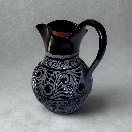 Black ceramic pitcher with intricate patterns on a gray background