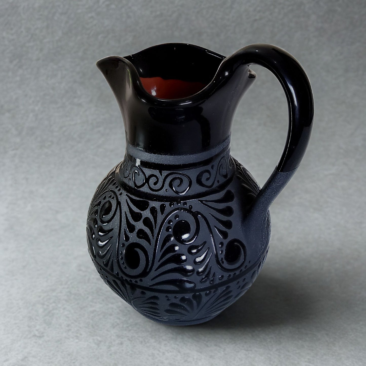 Black ceramic pitcher with intricate patterns on a gray background