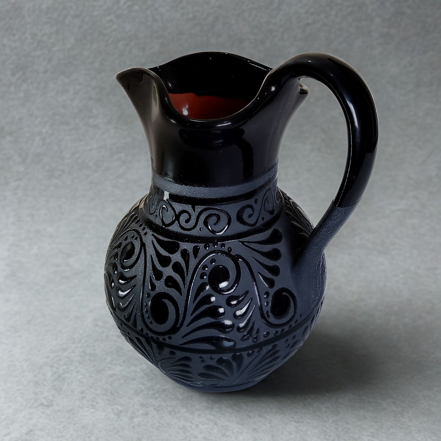 Black ceramic pitcher with intricate patterns on a gray background