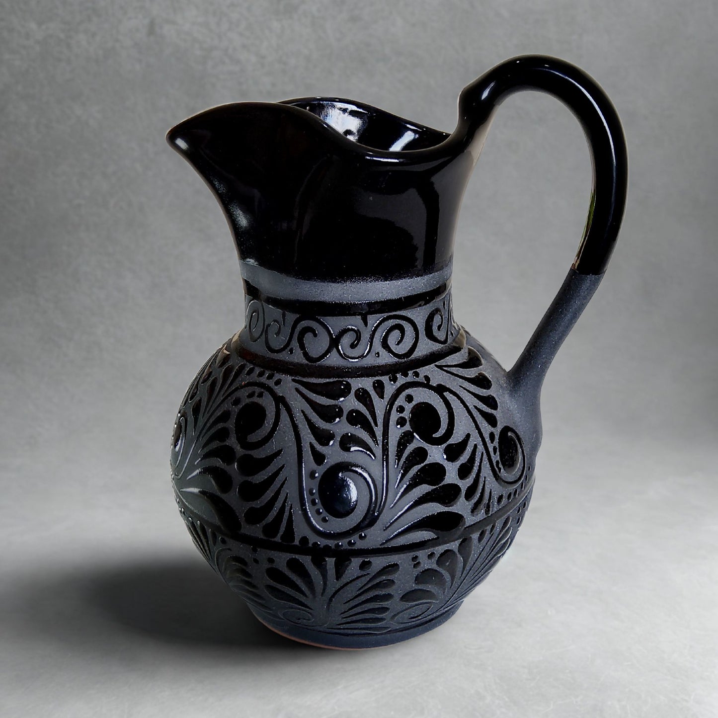 Black ceramic pitcher with intricate patterns on a gray background