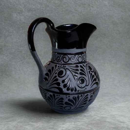 Black ceramic pitcher with intricate patterns on a gray background